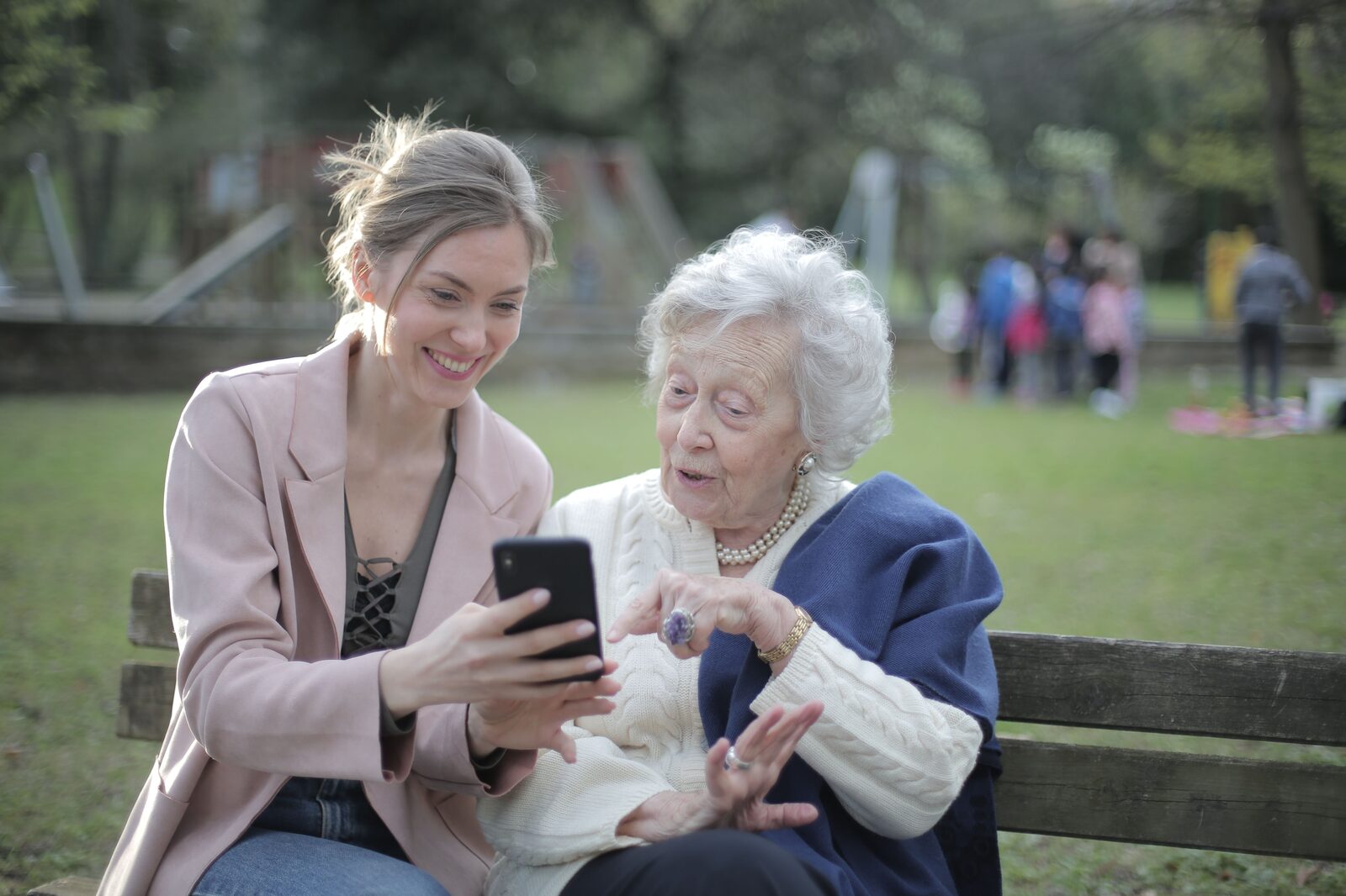 A younger woman and an older woman looking at a phone together on a park bench