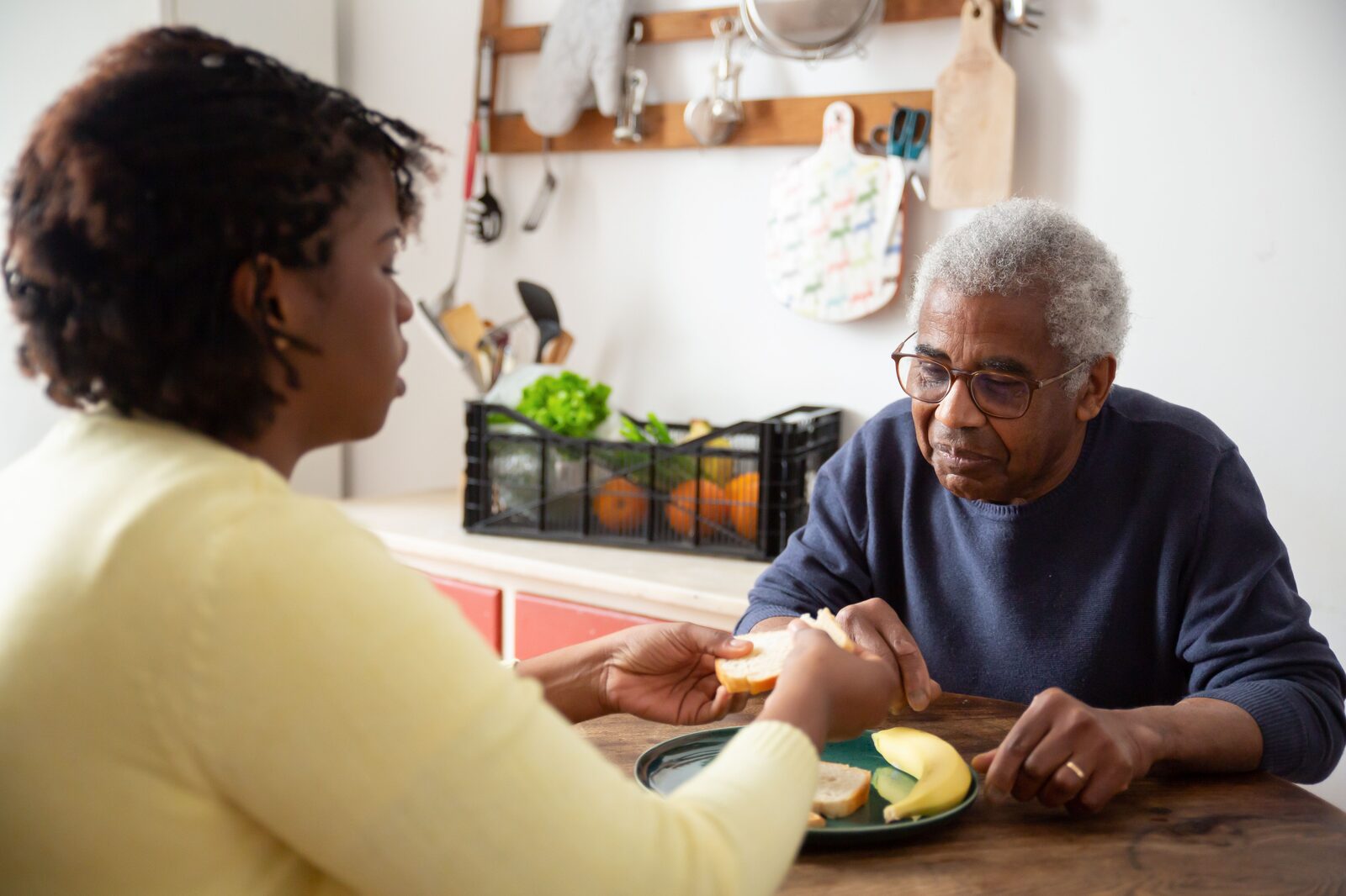 A caregiver helping an older man with a meal at a kitchen table