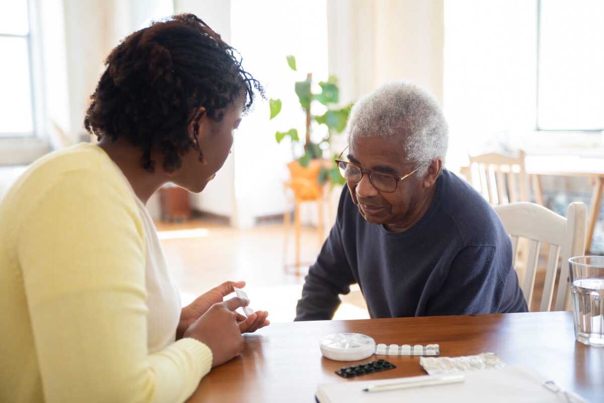 A woman and an older man talking across a wooden table at home