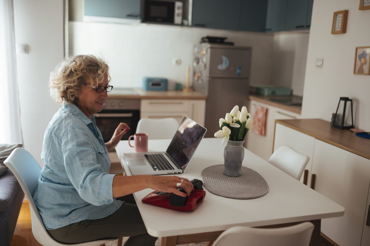 A woman at her kitchen table reviewing opportunities on a laptop